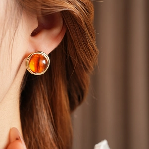 Close-up of amber resin earrings with gold trim on model ear in vintage style