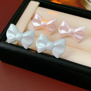 Detailed close-up of pearlescent bow stud earrings in blue and pink on a jewelry box