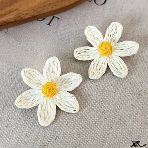 Detail shot of daisy-shaped raffia earrings on linen background with resort style vibes