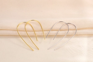 Dettaglio di orecchini a U minimalisti oro e argento su morbido tessuto beige