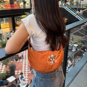 Orange crescent bag with floral embroidery worn on shoulder in a mall setting