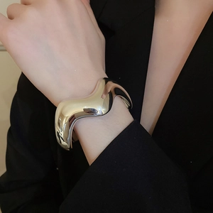 Dettaglio di un ampio bracciale in argento lucido con design minimalista a onde