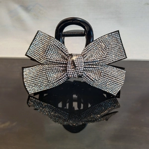Detailed view of the rhinestone-studded bow hair claw clip on a reflective black surface