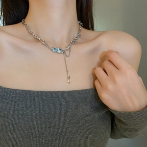 Detail of silver necklace with blue stones, thorn design, and transparent drop pendant