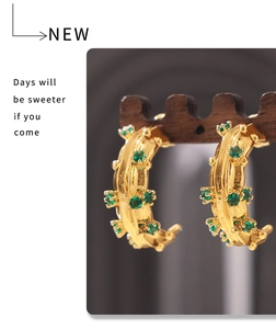 Detailed macro view of C-shaped 18k gold plated earrings with inlaid green glass stones