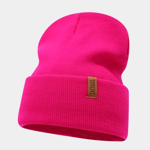 Detail of hot pink ribbed knit beanie featuring a brown leather patch with text
