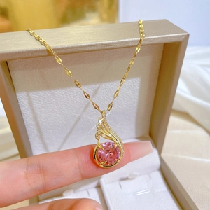 Elegant gold phoenix necklace with pink crystal pendant held by hand over a jewelry box