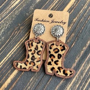Leopard print cowboy boot earrings with silver flower studs on a dark wood background