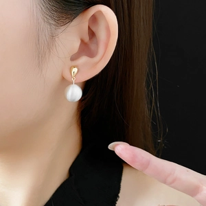 Gros plan de boucles d'oreilles minimalistes plaquées or avec une perle blanche mate sur un modèle