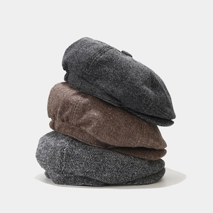 Macro shot of stacked herringbone newsboy caps in charcoal grey and warm brown tweed fabric