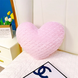 Détail d'un coussin en peluche rose en forme de cœur avec motif de vagues brodées
