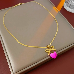 Détail d'un collier chaîne serpent dorée avec cœur rose et pendentif nœud sur un plateau