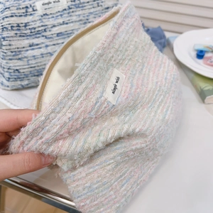 Detail of tweed makeup bag showing multi-color weave and simple wish brand label
