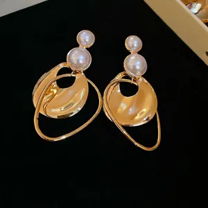Irregular gold geometric earrings with white pearls on a luxurious black velvet background
