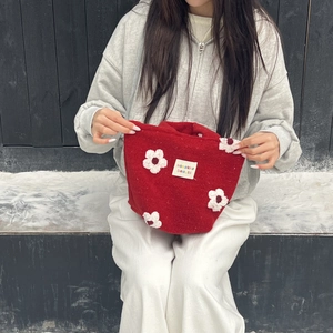Close-up of red plush bucket bag with white floral embroidery and woven brand label