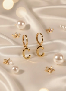 Macro shot of gold letter C pendant earrings displayed on elegant cream silk fabric