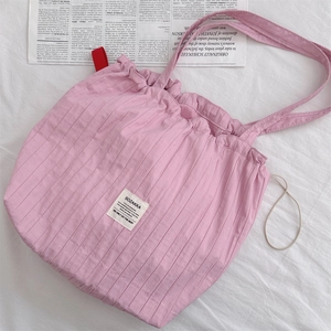 Detail of pink pleated tote bag with white branded label on soft fabric texture