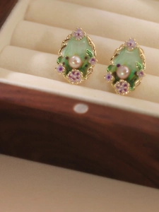 Macro detail of vintage floral earrings with green enamel and a pearl in a jewelry box