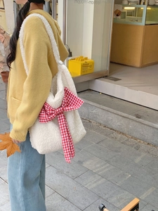Detail of white plush shoulder bag featuring a large red plaid bow in a street style shot
