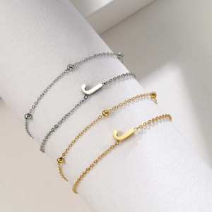 Detail of gold and silver layered chain bracelet with letter J charm on white display