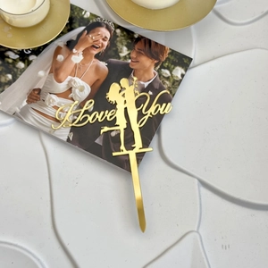 Close-up of golden acrylic I Love You cake topper with a kissing couple silhouette