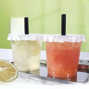 Close-up of thick transparent PET plastic cup with white wavy lid and black straw on metal tray
