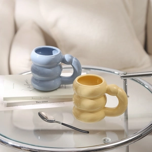 Close-up of blue and yellow ceramic mugs with unique wavy cloud design and handles