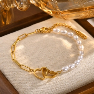 Detail of a gold heart charm and pearl asymmetrical bracelet on a linen background