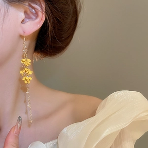 Close-up of elegant long gold tassel earrings with yellow flowers on a female model