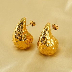 Macro detail of gold plated teardrop earrings with hammered texture on champagne silk