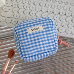 Detailed view of a blue and white checkered pouch with a pink rope zipper pull and woven label
