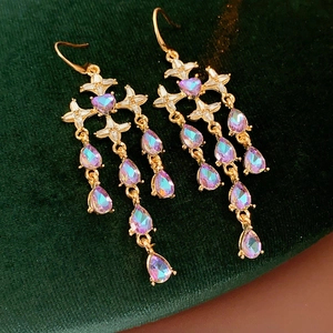 Macro detail of gold tassel earrings with purple crystals on dark green velvet