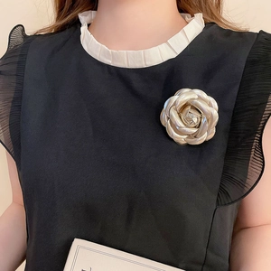 Detail of a champagne gold leather camellia brooch on an elegant black and white outfit
