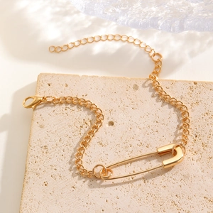 Detail of a gold safety pin bracelet on a beige stone base with elegant natural shadows