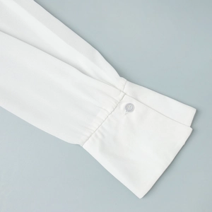 Detail of white chiffon shirt cuff featuring fine pleats and single button closure
