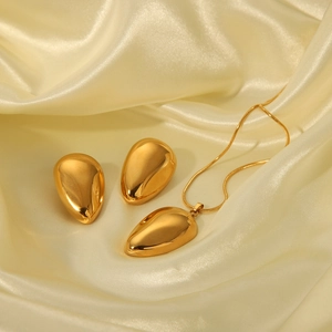 Macro shot of 18k gold-plated teardrop necklace and stud earrings on champagne silk fabric