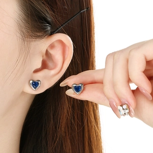 Detail of a silver heart stud earring with a dark blue stone on a model's ear