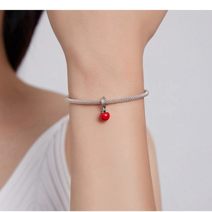 Close-up of a silver charm bracelet with a red apple pendant on a woman's wrist