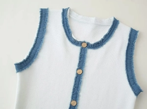 Close-up of white knit vest collar with blue raw-edge denim trim and gold metal buttons