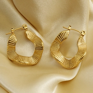 Macro shot of 18K gold-plated textured wavy earrings on champagne silk fabric surface