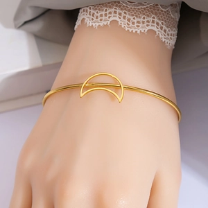 Detail of gold moon crescent open bangle worn on wrist with elegant lace sleeve accent