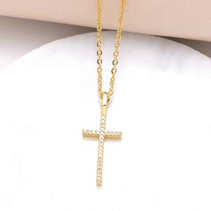 Gold plated cross pendant necklace with white zircon crystals on a white stone pedestal