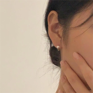 Close-up of elegant silver four-pointed star stud earring on a female model's ear
