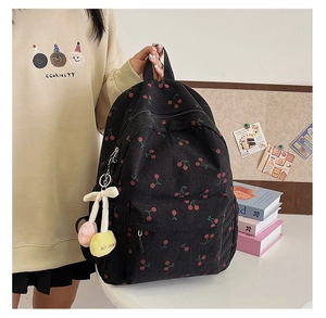 Detail of black corduroy backpack featuring red cherry prints and a plush cherry pendant