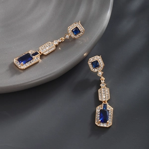 Macro detail of luxury gold-tone earrings with blue rectangle crystals and tiny zircon accents