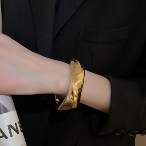 Gros plan d'un bracelet géométrique doré épais porté sur une veste de costume noire
