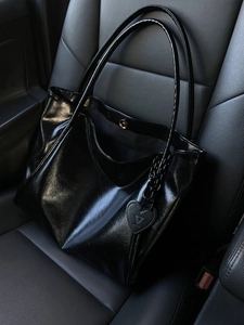 Black glossy leather tote bag with heart charm on a car seat for daily commuting