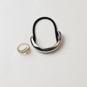 Close-up of a polished silver crescent hair tie and gold crisscross ring with micro-pave stones