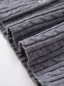 Detailed close-up of gray cable-knit sweater texture with decorative gemstone button detail