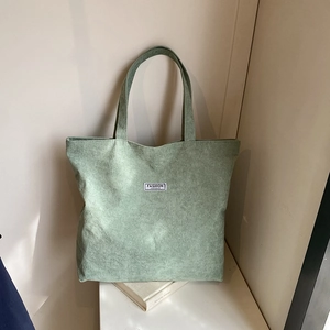 Detail of mint green corduroy tote bag featuring a minimalist fashion label on white books